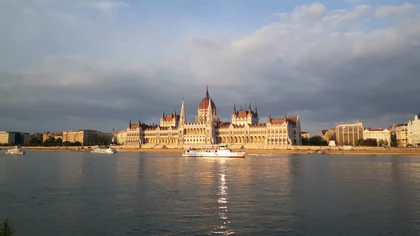 The Hungarian Parliament Building (Parliament of Budapest) in the evening with a cruise ship and sun reflection