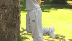 Man in sportswear stretching against a tree in a park