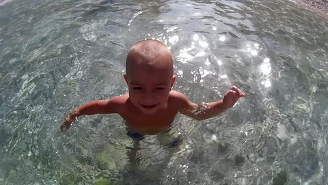 Twenty months' old toddler swims underwater in the sea then a hand helps him out, taken by action camera
