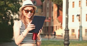 Woman using digital tablet and drinking coffee in the European city. Slow Motion, 4K. Hipster girl browsing Internet, searching for maps and information, communicating outdoors. Travel.