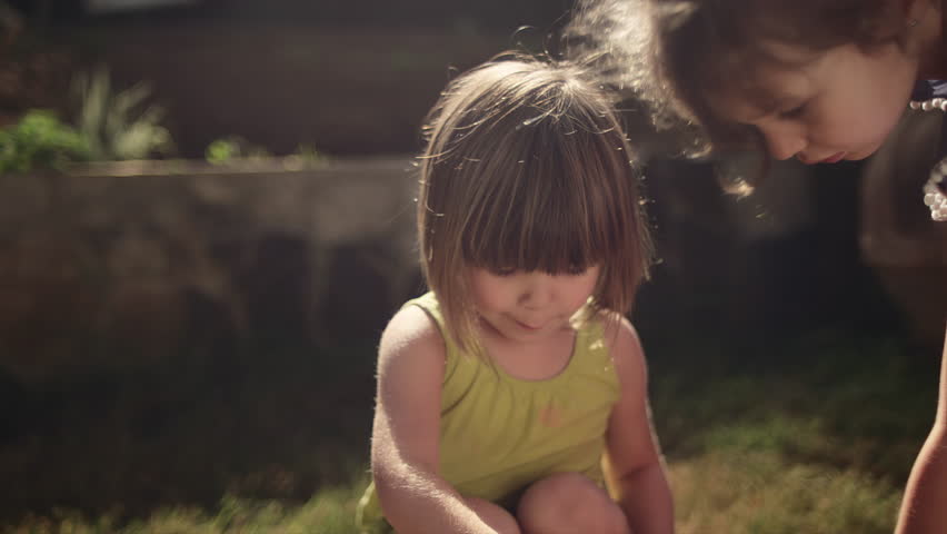 A little girl blows bubbles and her sister comes to help her