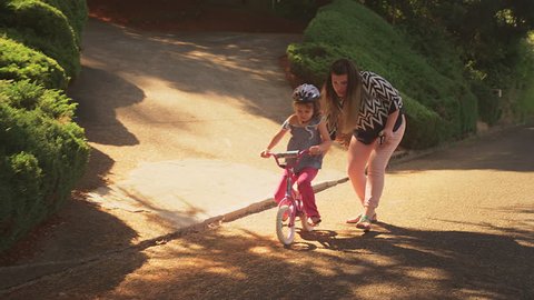A mother helps her nervous daughter get started on her bicycle and the girl takes off