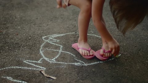 A little girl drawing a circle around her feet with chalk