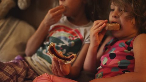 A little girl puts a donut up to her sister's face and leaves jelly on her nose