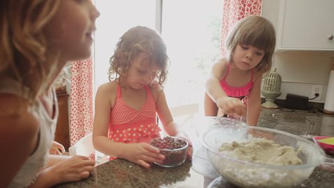 Three little girls helping their mother bake by adding chocolate chips