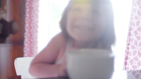 A cute little girl sitting at a kitchen counter with a bowl in front of her