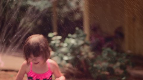 A cute little girl playing outside in a sprinkler