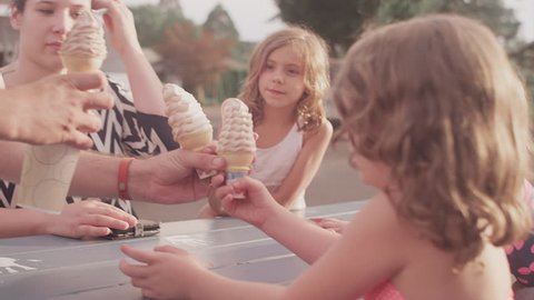 A father hands out ice cream cones to his kids at a picnic table
