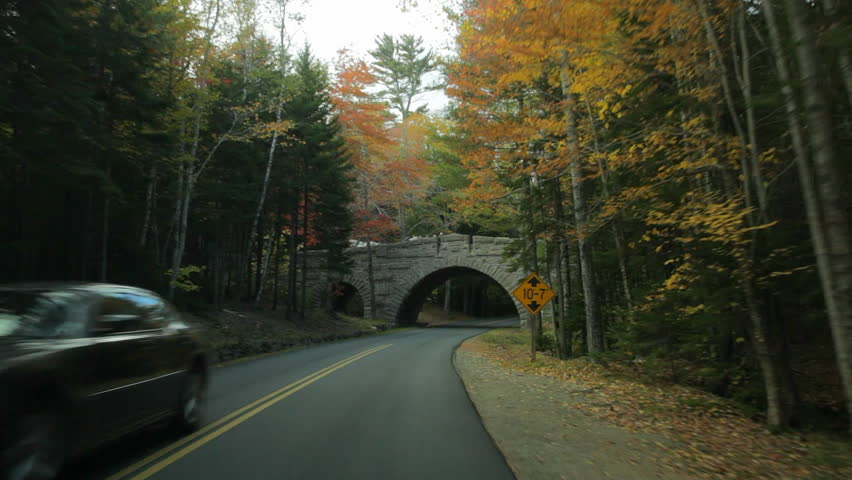 Driving on Stanley Brook Road passing under Stanley Brook Bridge with a horse-drawn carriage crossing on it, in Acadia National Park in Autumn. 