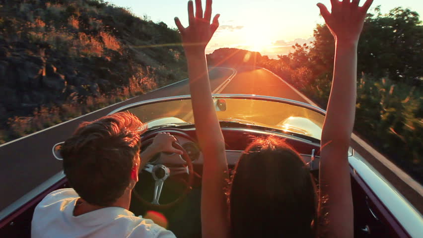 Couple driving convertible car. steadicam shot with flare into sunset in Hawaii