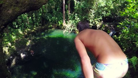 SLOW MOTION. Young Man Jumps off Cliff Into Water. Summer Extreme Sports Outdoor Lifestyle. Lush Green Jungle.