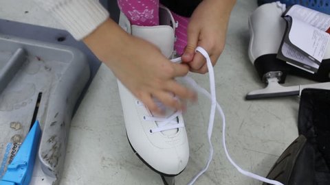 A girl ties the laces on white skate in the store, visible only hands and leg