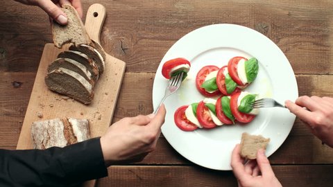 Caprese salad on white plate with bread on cutting board - meal preparation and time-lapse eating on wooden table - stop motion animation