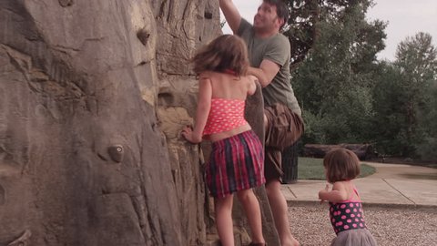 A father and daughter climb up a rock wall at a park