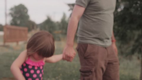 A little girl and her dad walk hand in hand down a park trail
