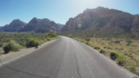 Viewpoint of a motorcyclist riding in Nevada Red Rock Canyon in 4K format. A biker rides down a scenic and empty road toward the mountains.