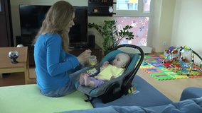 zoom in of little baby eat vegetable porridge in car seat with mother in living room. Static tripod shot. 4K UHD video clip.