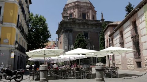 Madrid, Spain - June 2015:  People enjoy drinks or a meal sitting outside under sunshades with waiters in attendance near to the Iglesia De San Andres