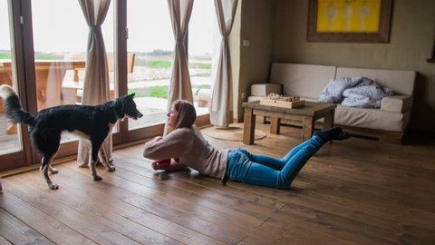 Woman lay on floor and play with dog 4K. Wide shot of living room in old traditional home with big futuristic bright windows and couch in background. Cute puppy and attractive female person.