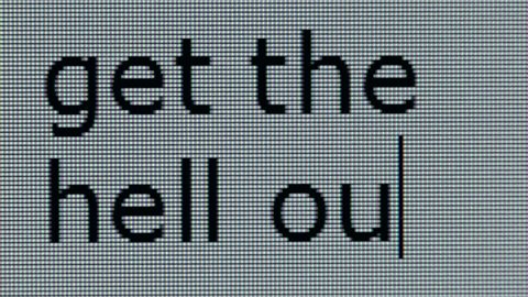 "get the hell out" being typed on computer screen in close up so that individual pixels can be seen.