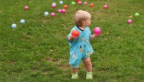 Video baby taking its first steps. Child with a color ball goes over the grass lawn.