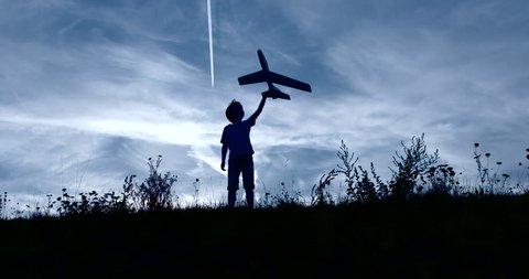 Boy playing outside with toy airplane silhouetted slow motion