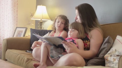 A mother reads a book to her daughters on the couch