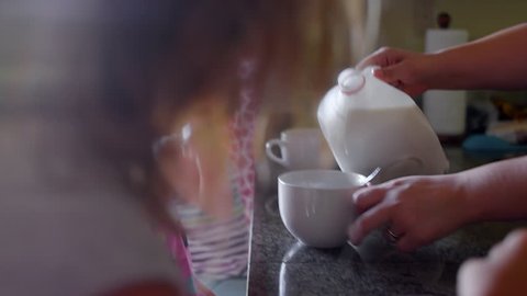 A mother pours milk into her daughters' cereal bowls