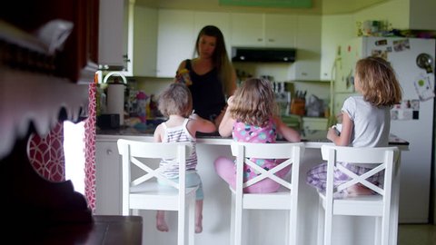 A mother talks to her daughters at the kitchen counter in the morning