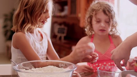 Little girls at a kitchen counter helping their mom bake