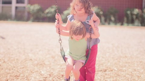 A girl pushing her younger sister on a swingset