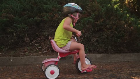 An adorable little girl happily riding her tricycle