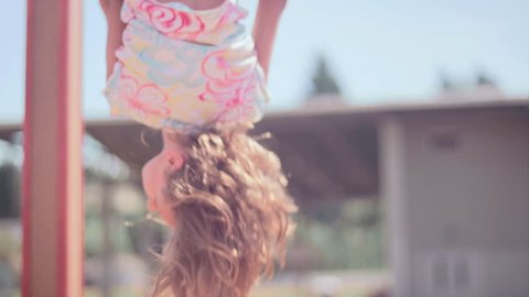 A girl hangs upside down from monkey bars and then jumps down and smiles