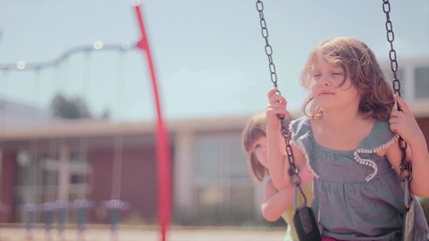 A girl struggles to push her older sister on a swingset