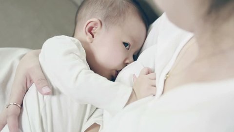 Young mother breast feeding her infant on couch at home, New family and baby protection from mom concept