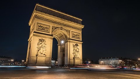 A Time Lapse of the of the Arch of Triumph (Arc de Triomphe) by night, with cars and buses passing by with motion blur.
