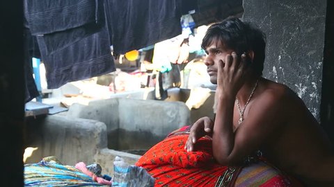 MUMBAI, INDIA - 10 JANUARY 2015: Man sitting and calling on the phone in a slum in Mumbai.