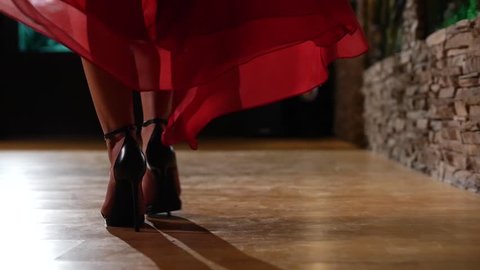 Female model in heels and red dress walking across wood floor