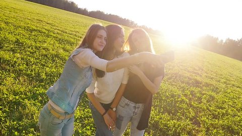 Three friends, young pretty girls, caucasians, having fun outdoors in fields on sunset, making selfie, slow motion.