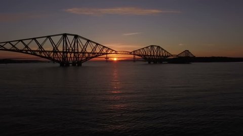 Stunning aerial shot of the Forth Rail Bridge during sunset in South Queensferry with a local train passing