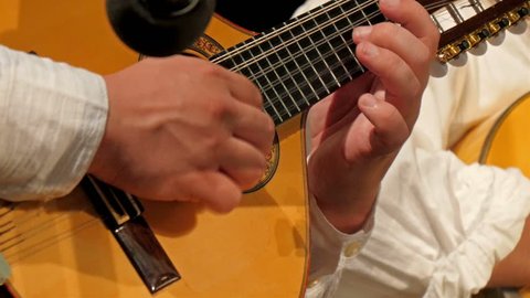 A brown ukelele or small guitar instrument. A man is strumming the guitar strings using his hand