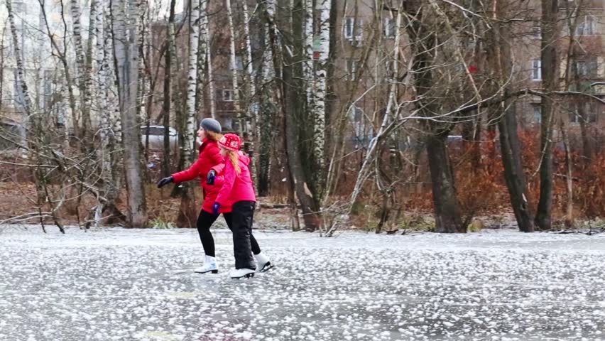 Girl and young woman in red skating on pond among trees