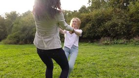 Two friends, young pretty girls, caucasian and african, having fun outdoors in park, spinning around in roundelay, slow motion.