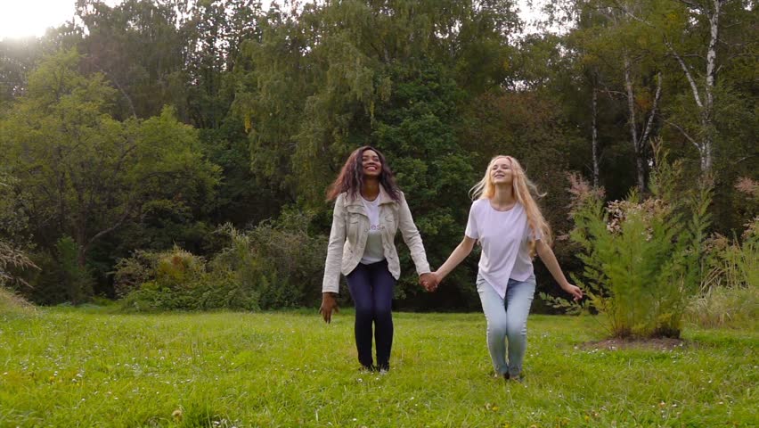 Two friends, young pretty girls, caucasian and african, having fun outdoors in park, jumping up, slow motion. | Shutterstock HD Video #11519288