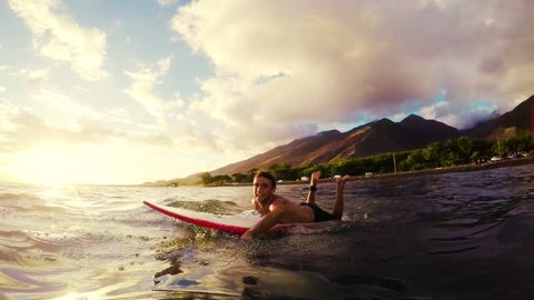 Young Man Paddles a Surfboard Through Golden Sunset in the Blue Ocean in Hawaii in Slow Motion. Instagram Filter Sun Flare. POV Point of View.