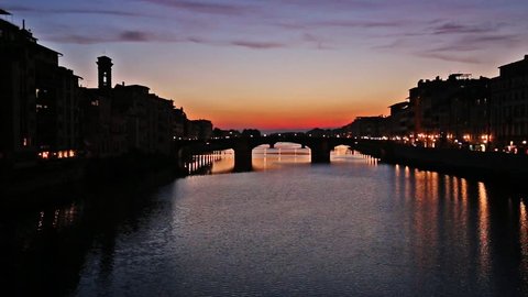 The Arno River, Florence, Tuscany, Italy. View of river and bridges at sunset with flickering lights and vivid colors reflected in water.