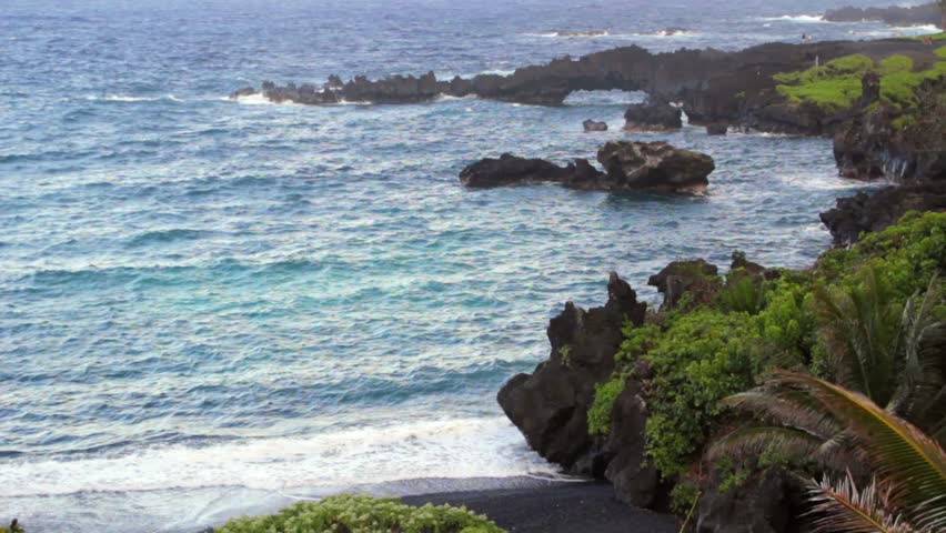 A black sand beach with an eroded sea arch in the distance