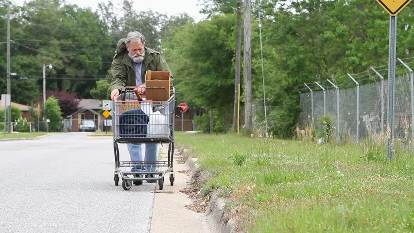 Homeless veteran pushes a shopping cart that holds his belongings down the side of the street. Royalty-Free Stock Footage #1157095
