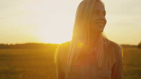 Smiling Blond Girl is Walking on Field at Sunset. Shot on RED Cinema Camera in 4K (UHD).