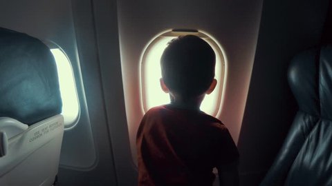 A young boy sitting on the seat looking out an airplane window while flying